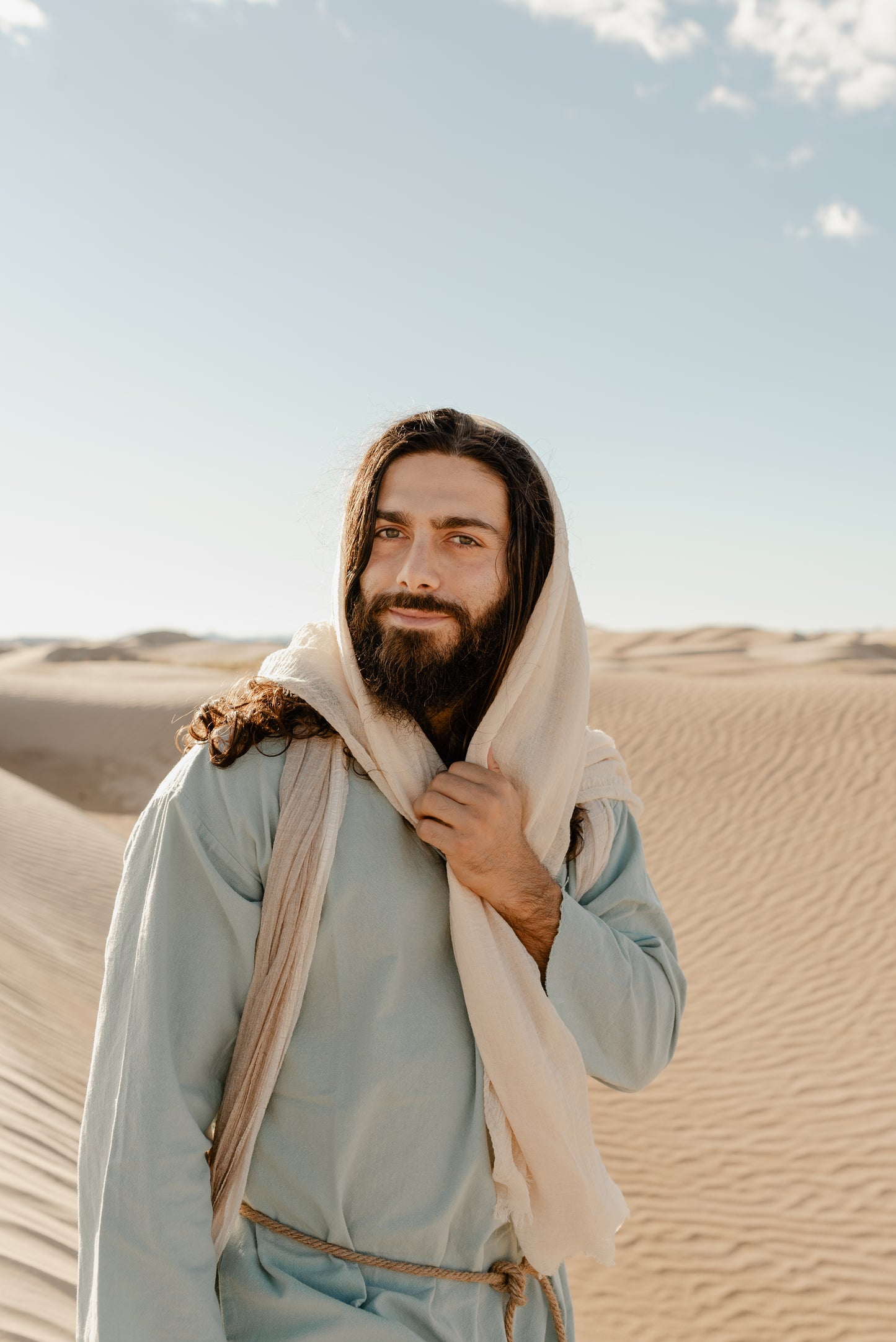 Image of Jesus Christ stading in light colored sand dunes wearing a scarf over his hair